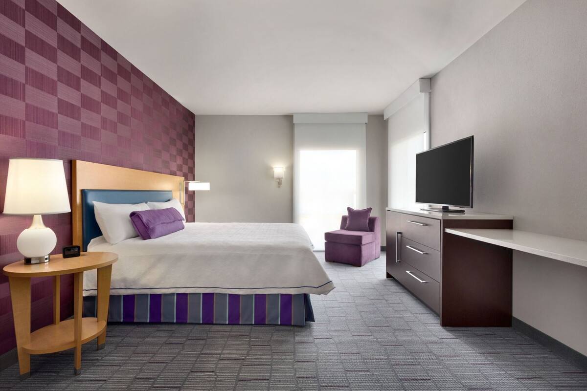 A hotel room with a bed, a desk, a television, a chair, and a lamp.