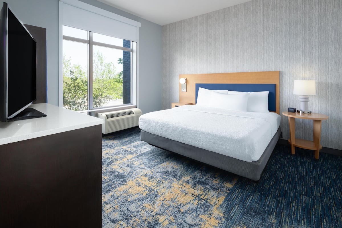 A hotel room with a large bed, a flat-screen TV, a desk, and a window with a view of trees.