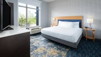 A hotel room with a large bed, a flat-screen TV, a desk, and a window with a view of trees.