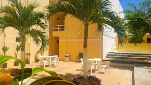Un patio con mobiliario exterior, palmeras y un edificio amarillo con una escalera.