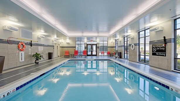 An indoor swimming pool with clear water, tiled walls, and red chairs along the sides.