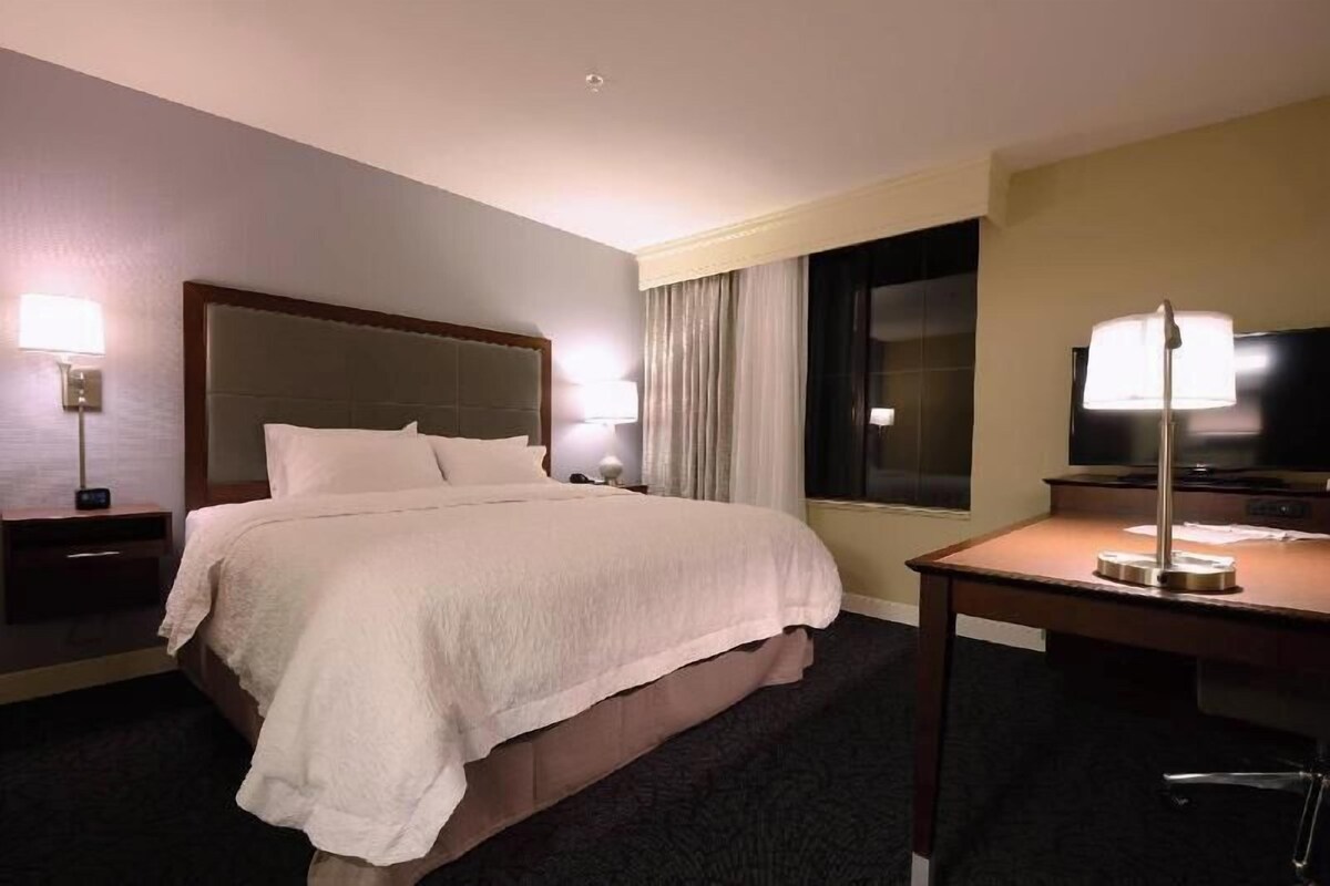 A hotel room with a bed, bedside tables, lamps, a desk, and a television.