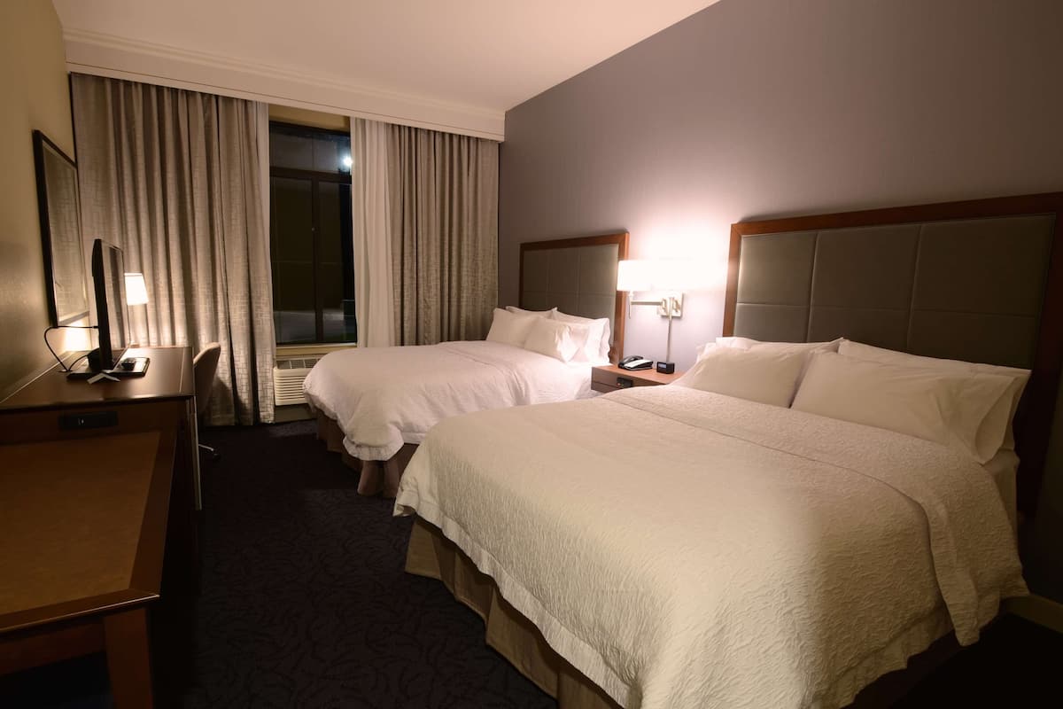 Une chambre d’hôtel avec deux lits, un bureau, une chaise et une fenêtre avec des rideaux.