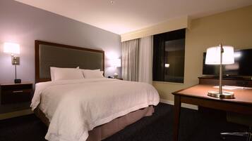 Una habitación de hotel con una cama grande, dos mesitas de noche con lámparas, un escritorio con lámpara, un televisor y una ventana con cortinas.