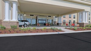 A hotel entrance with a covered driveway, a parking area, and outdoor seating.