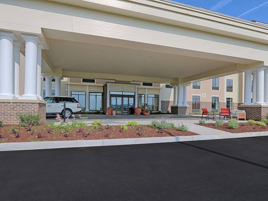 Entrada de un hotel con un camino cubierto, zona de estacionamiento y mobiliario exterior.