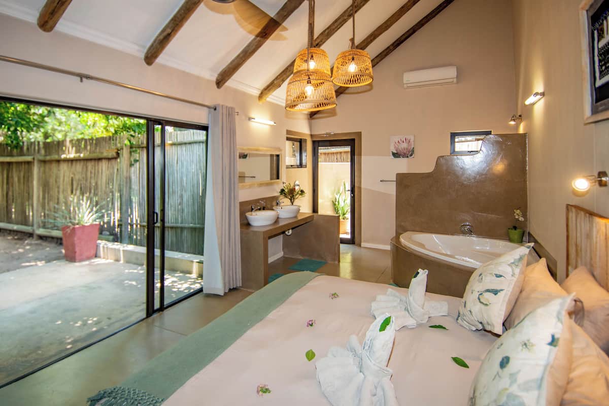 Un dormitorio amplio con una cama grande, un baño con bañera y un ventanal corredero que da a un patio.
