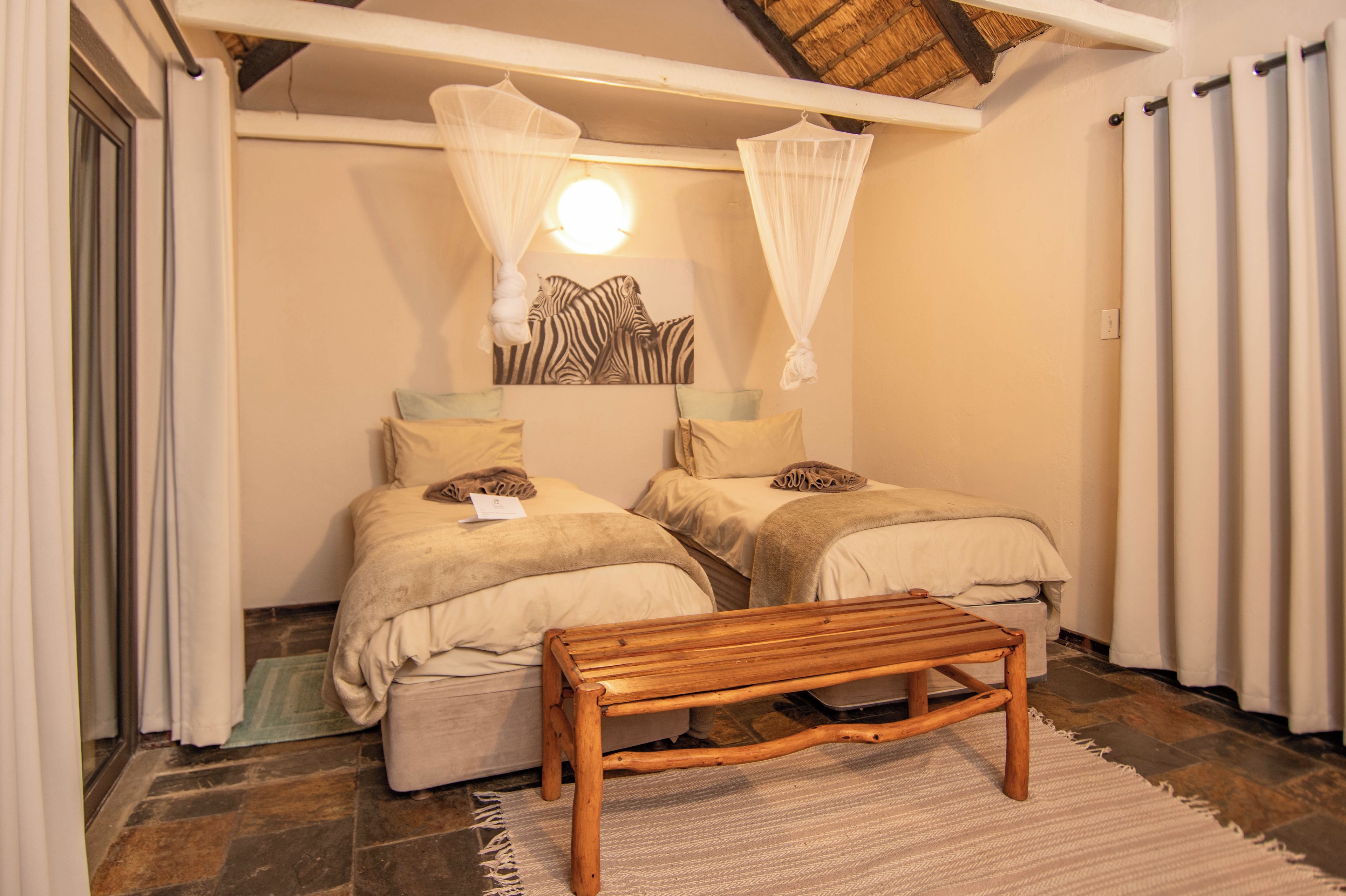 A room with two beds, a bench, and a canopy bed with mosquito netting.