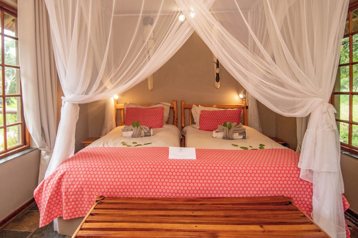 Una cama con una colcha roja estampada, cortinas blancas y un cabecero de madera.
