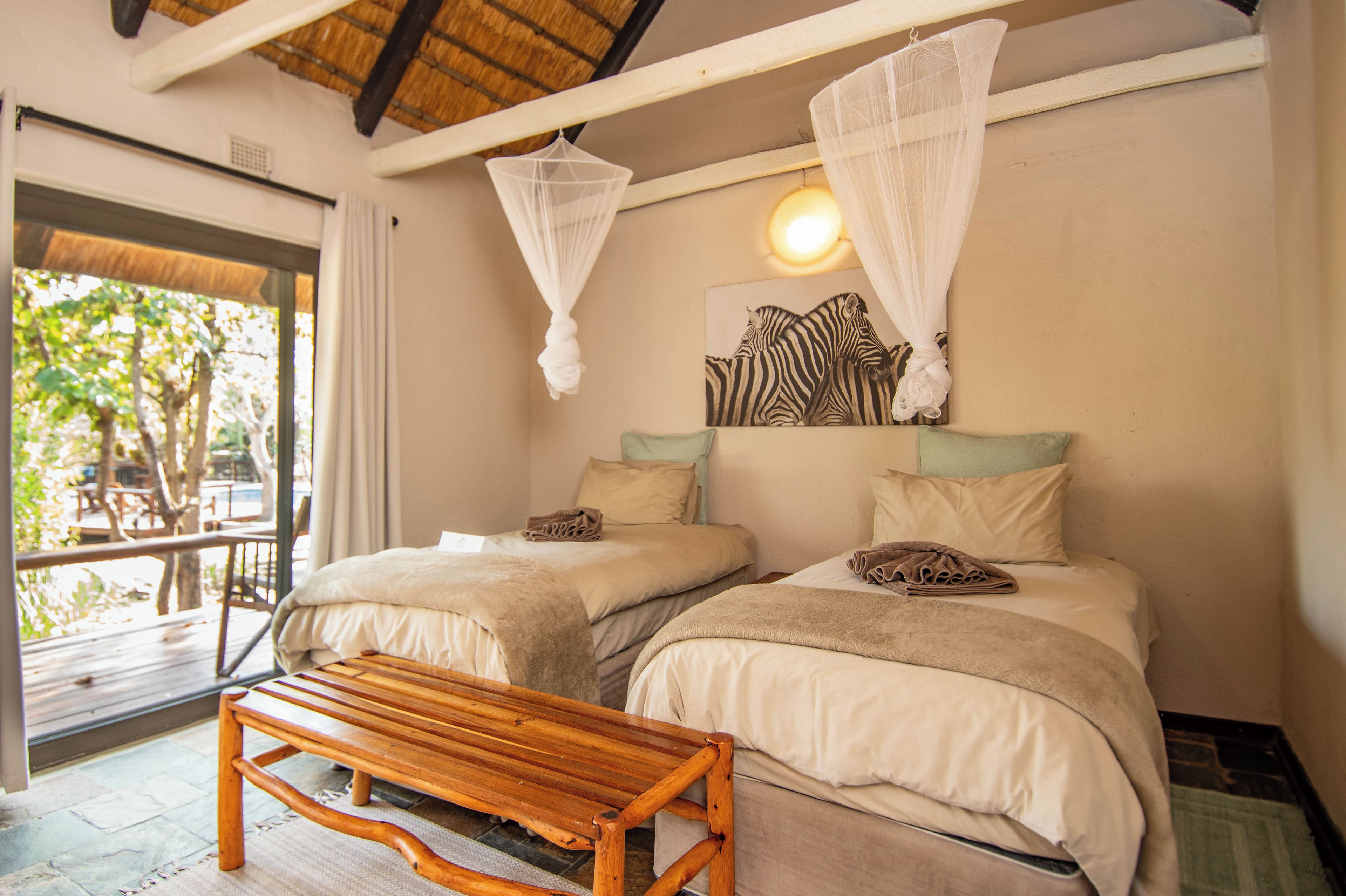 A bedroom with two beds, a bench, a zebra painting, and a window with a view of trees.