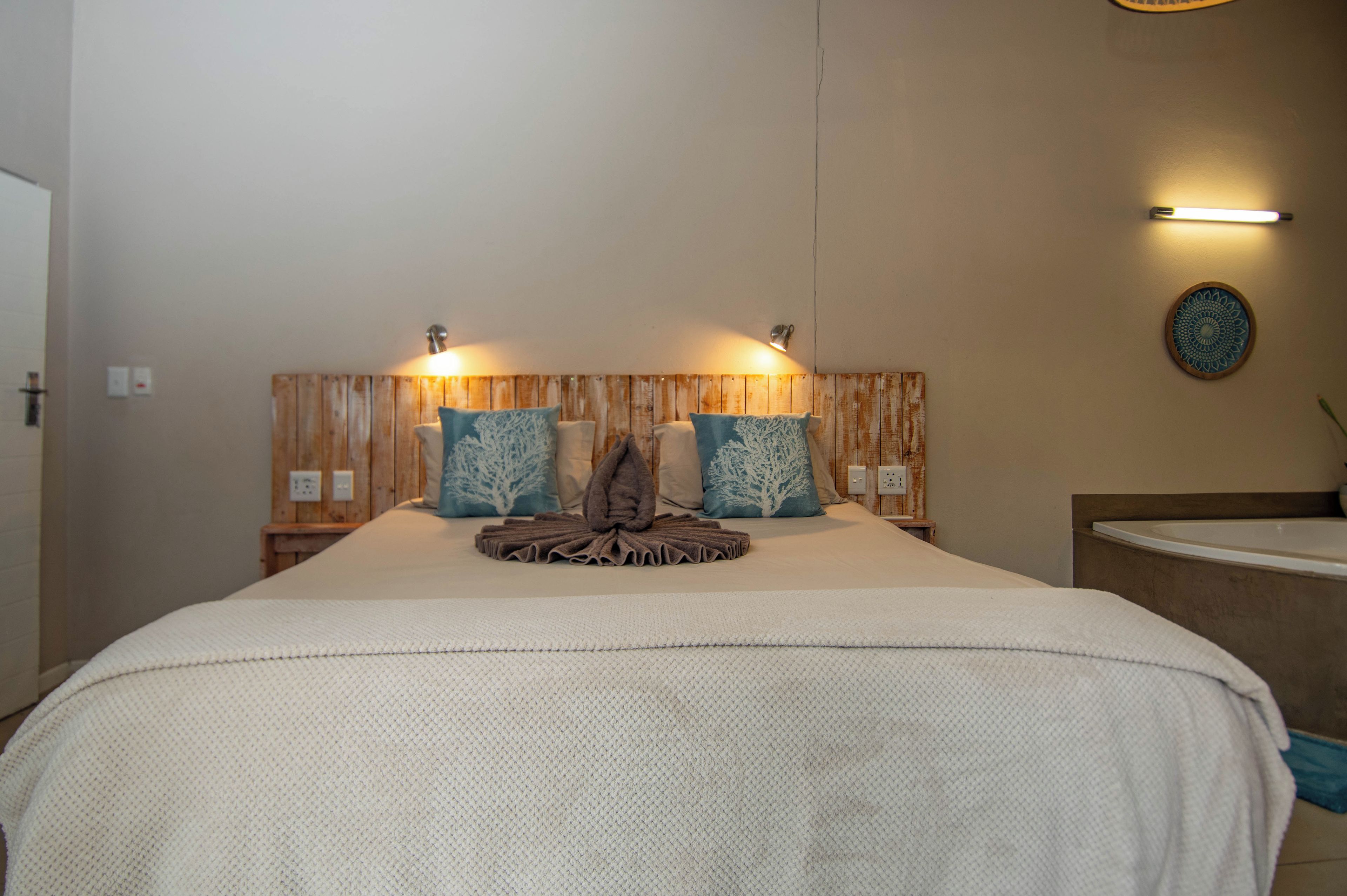 A hotel room with a large bed, wooden headboard, two wall-mounted lights, and a decorative wall piece.
