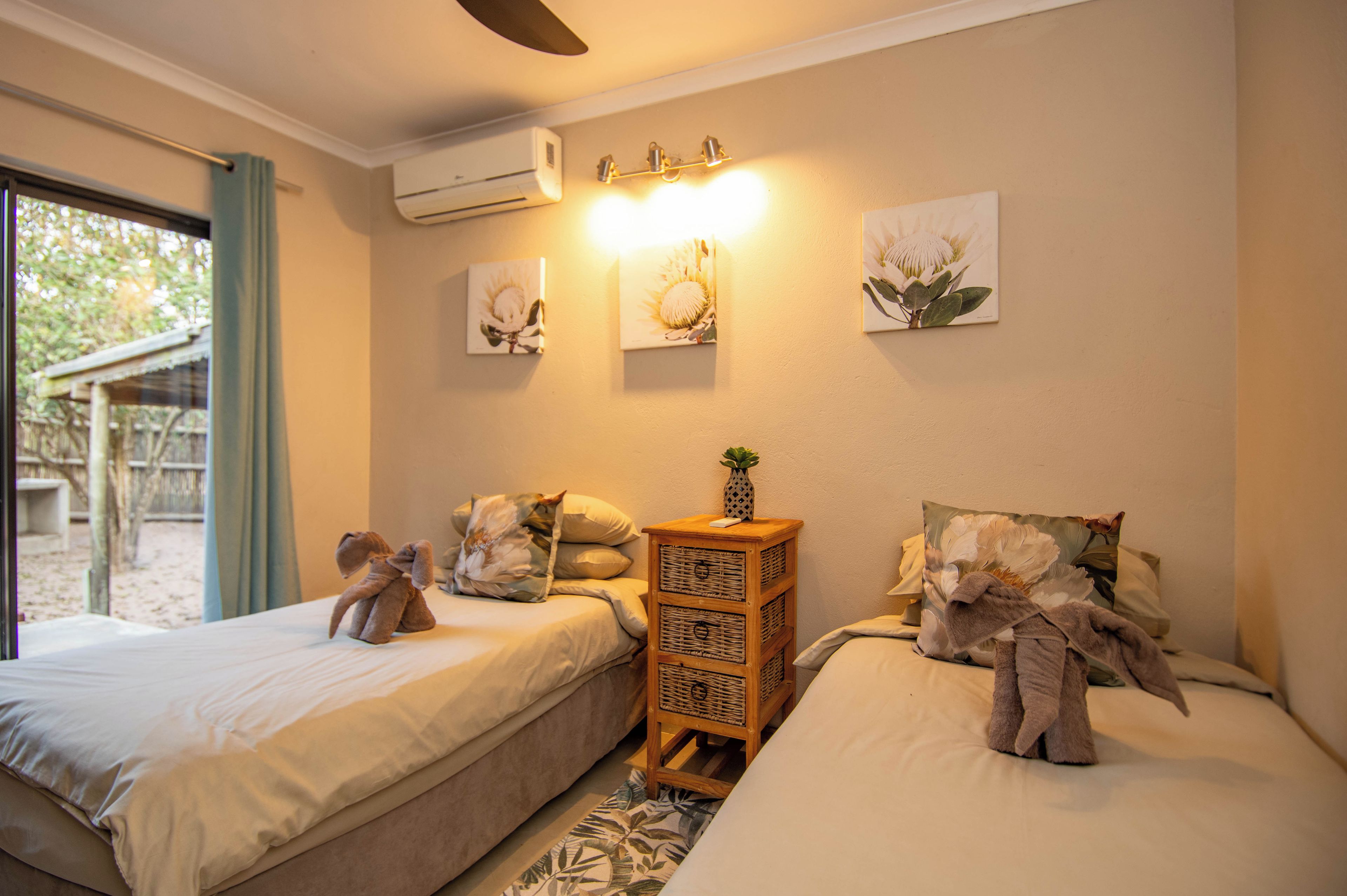 A room with two beds, a small wooden nightstand, and wall-mounted artwork.