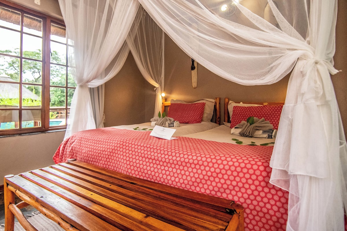 Un dormitorio con una cama, un banco de madera y un ventanal con vistas a la vegetación.
