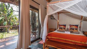 A wooden four-poster bed with a red patterned bedspread, a wooden headboard, and two pillows with elephant designs.