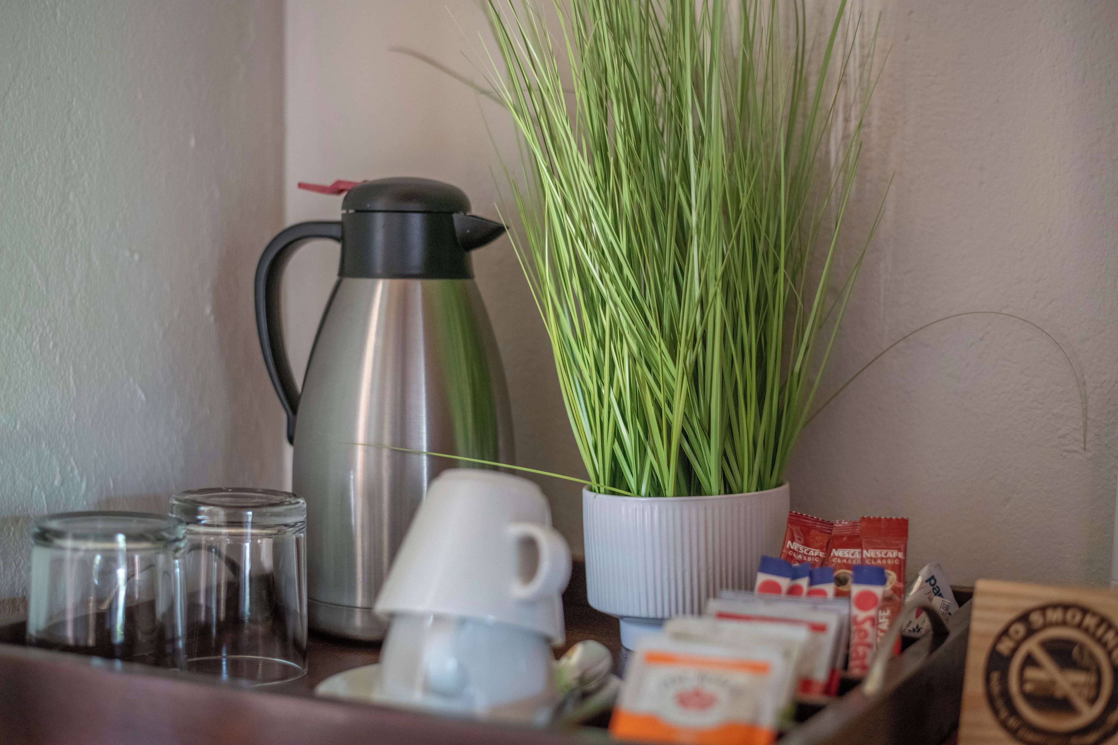 A kitchen counter with a coffee maker, a potted plant, a cup, and some coffee packets.