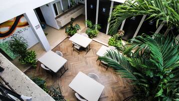 An indoor space with multiple tables and chairs, surrounded by various plants and a herringbone-patterned floor.
