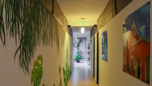 Un pasillo con un mural de plantas a la izquierda, una lámpara en el techo y una puerta al final.