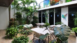 Un jardín interior con mesas y sillas, rodeado de plantas diversas.