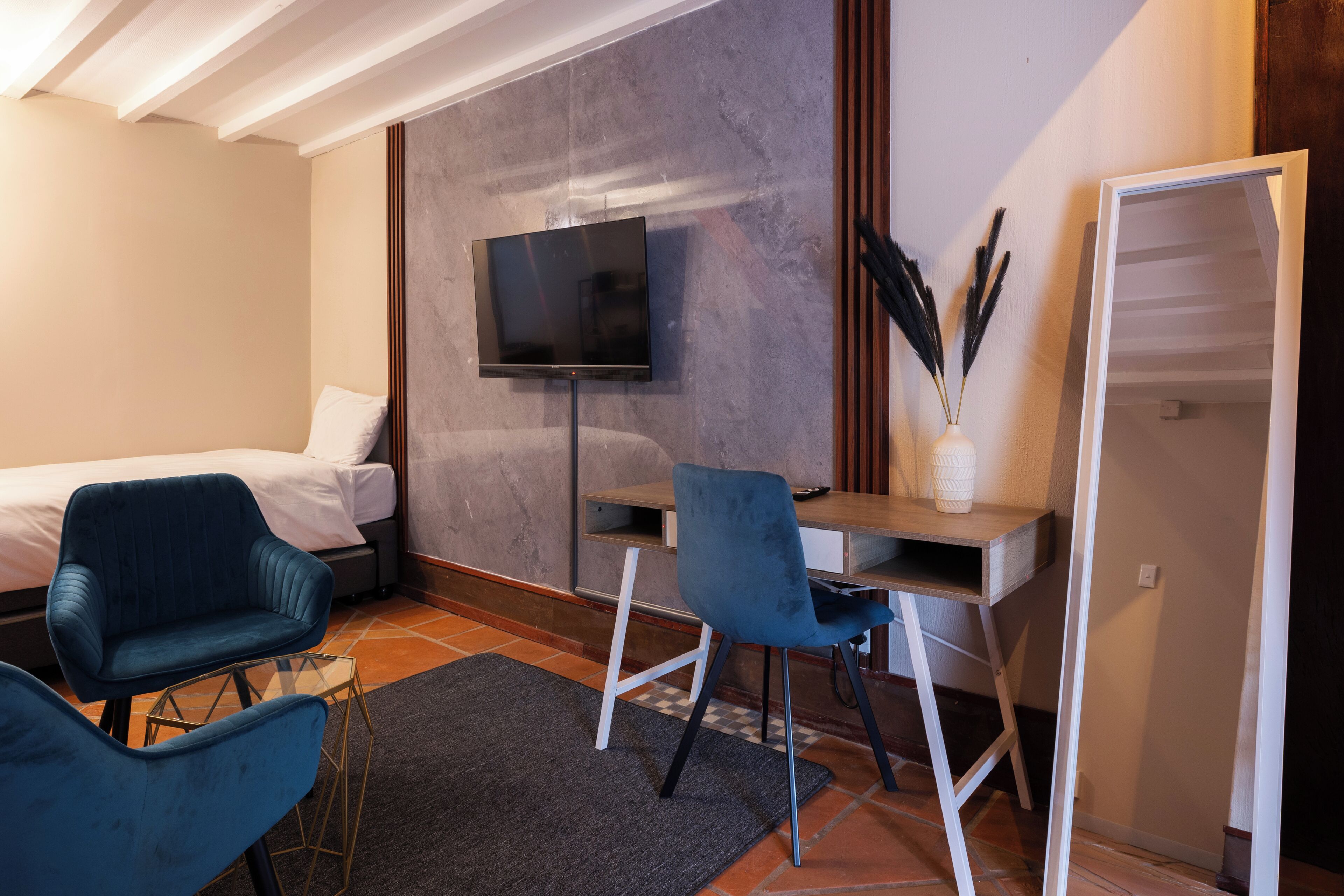A bedroom with a bed, a desk, a chair, a TV, and a vase with decorative items.