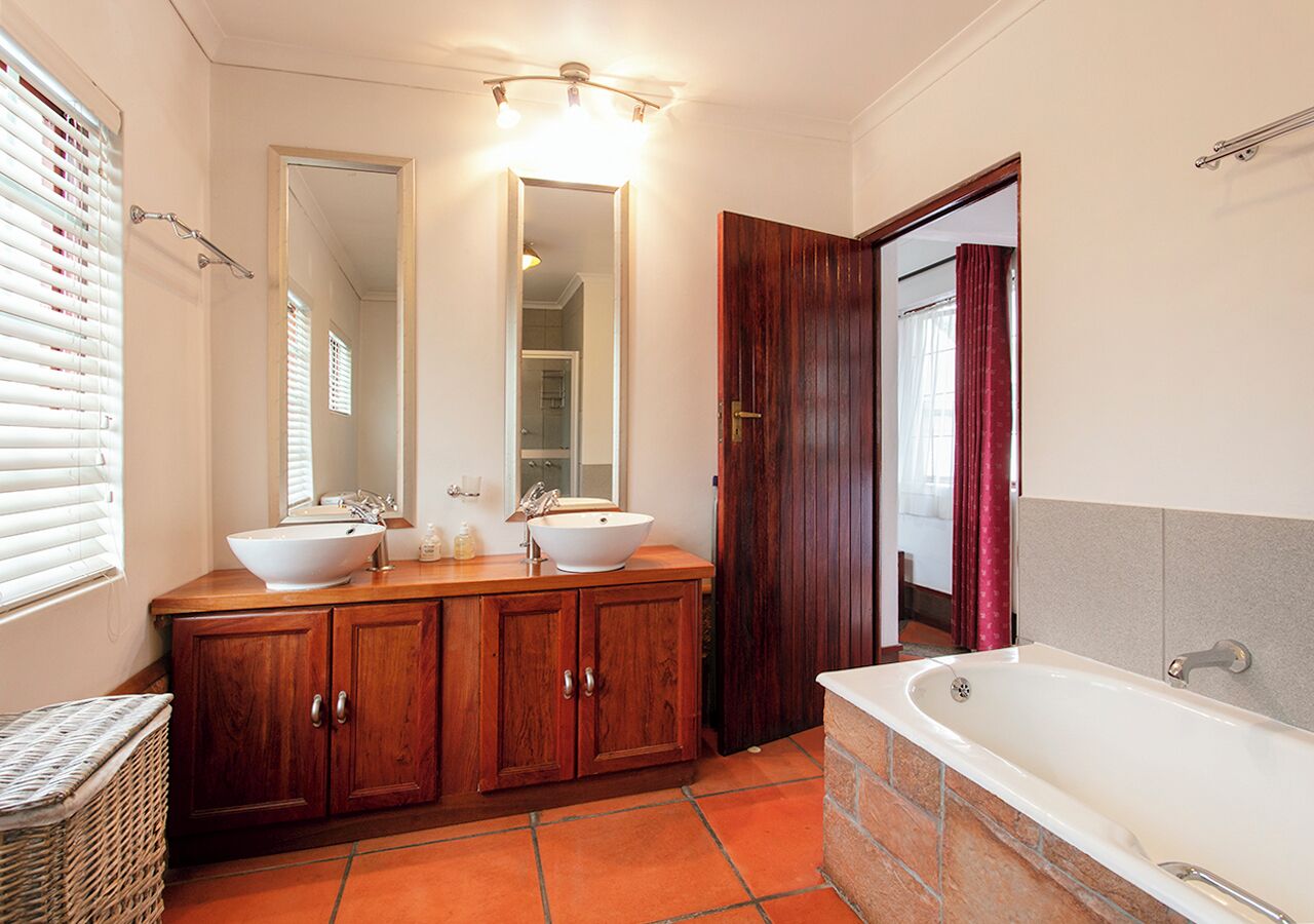 Ein Badezimmer mit einem Doppelwaschbecken, einem großen Spiegel, einer Holzwaschkommode, einer Badewanne und einem Korbwannenstuhl.