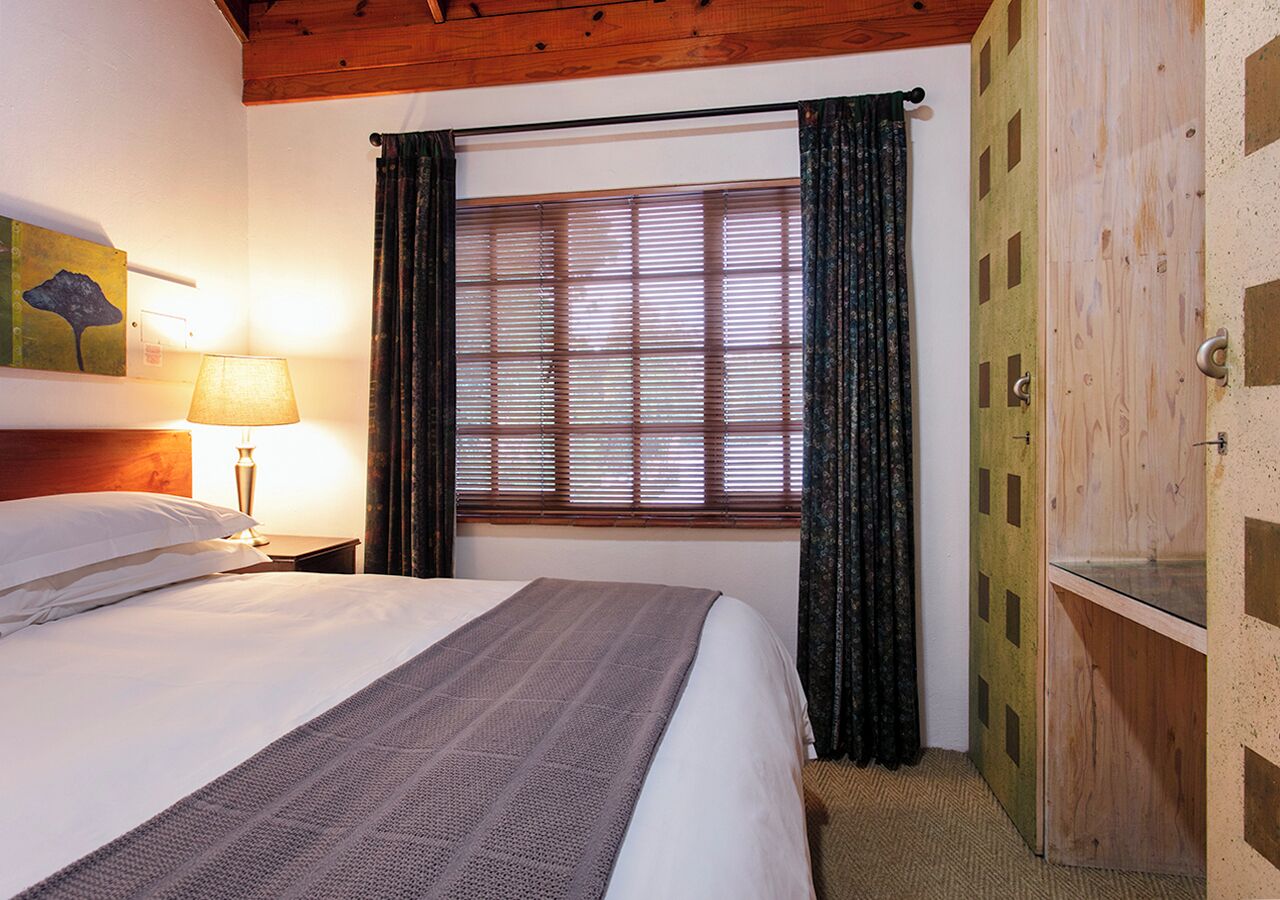 Une chambre à coucher avec un lit, des rideaux, une fenêtre, une table de chevet avec une lampe et une armoire en bois.