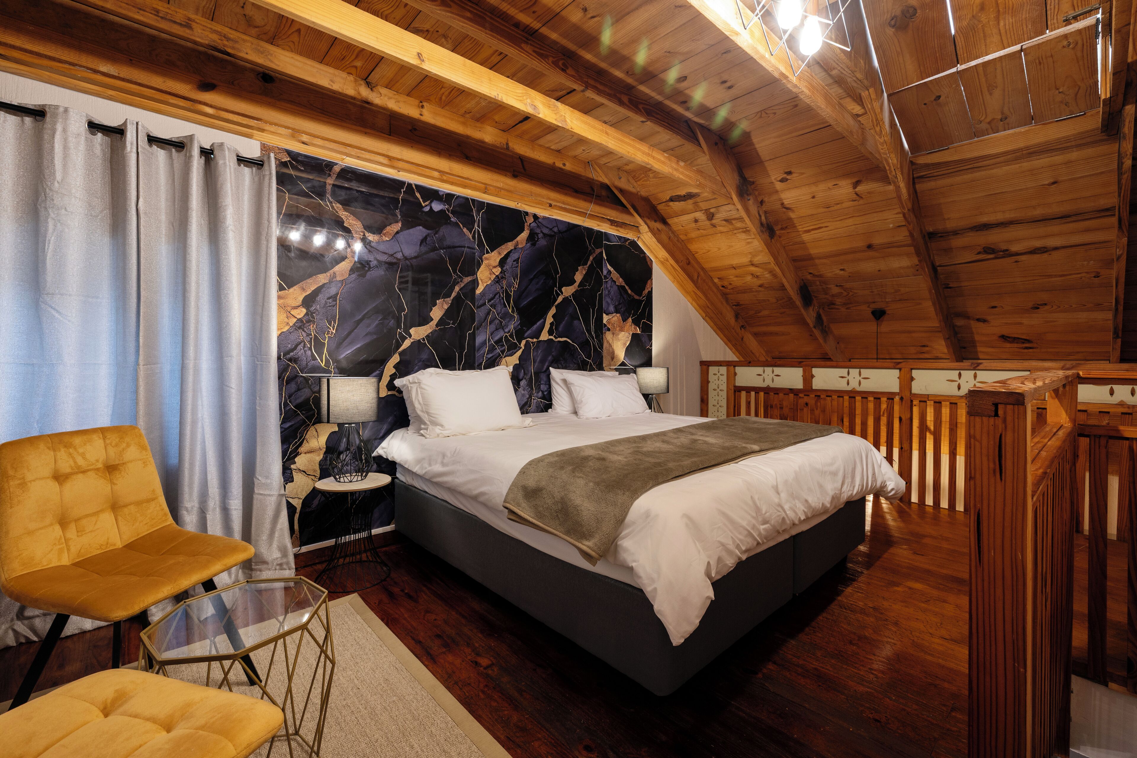 A bedroom with a bed, a chair, a nightstand, and a wall with a marble-like design.