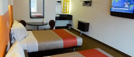 A hotel room with two beds, a desk, a chair, a small table, a mirror, a TV, and a bathroom.