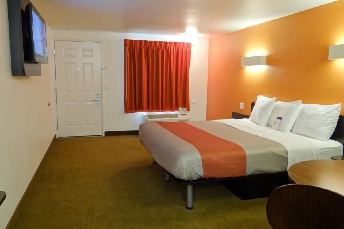 Una habitación de hotel con cama, escritorio, silla, televisión instalada en la pared y puerta.