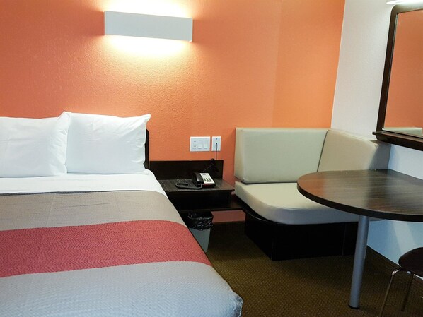 Habitación de hotel con cama, una mesita, una silla, un sofá y una lámpara en la pared.
