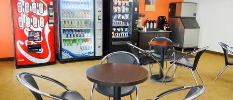 A room with vending machines, including Coca-Cola and Aquafina, and a coffee machine. There are tables and chairs for seating.