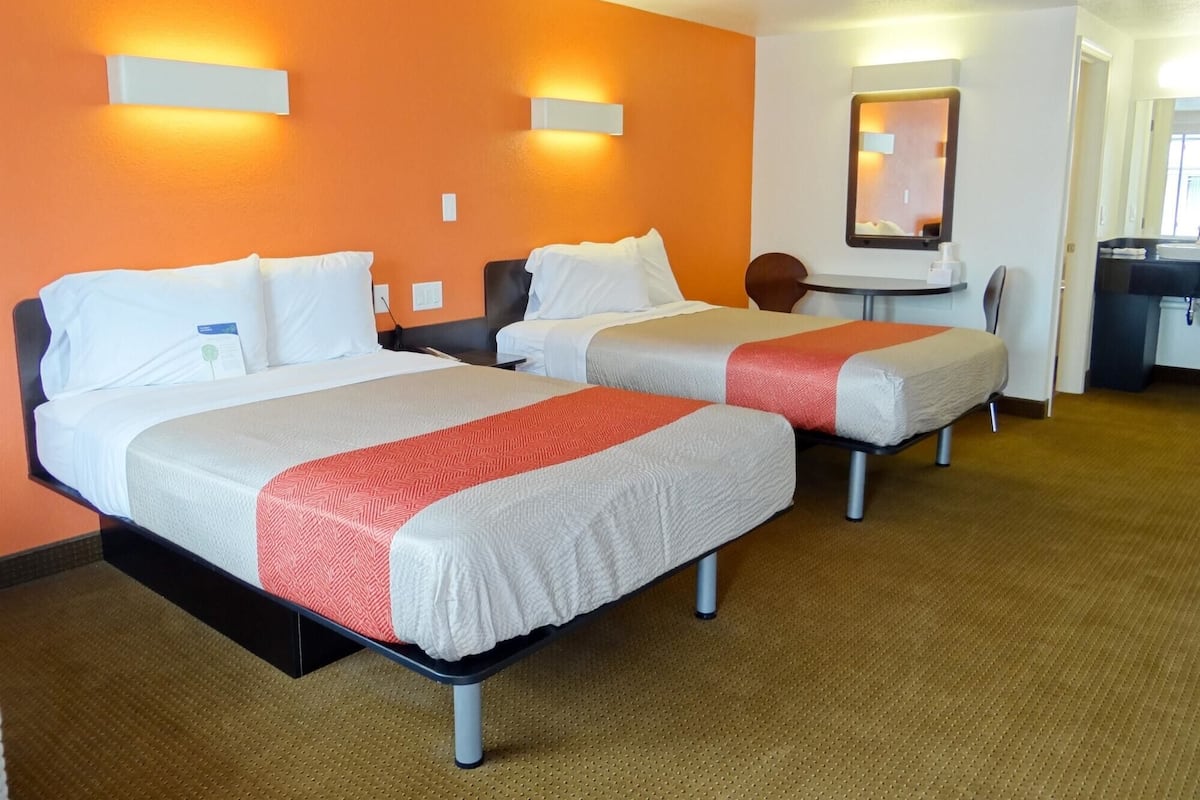 A hotel room with two beds, a small table, and a mirror.