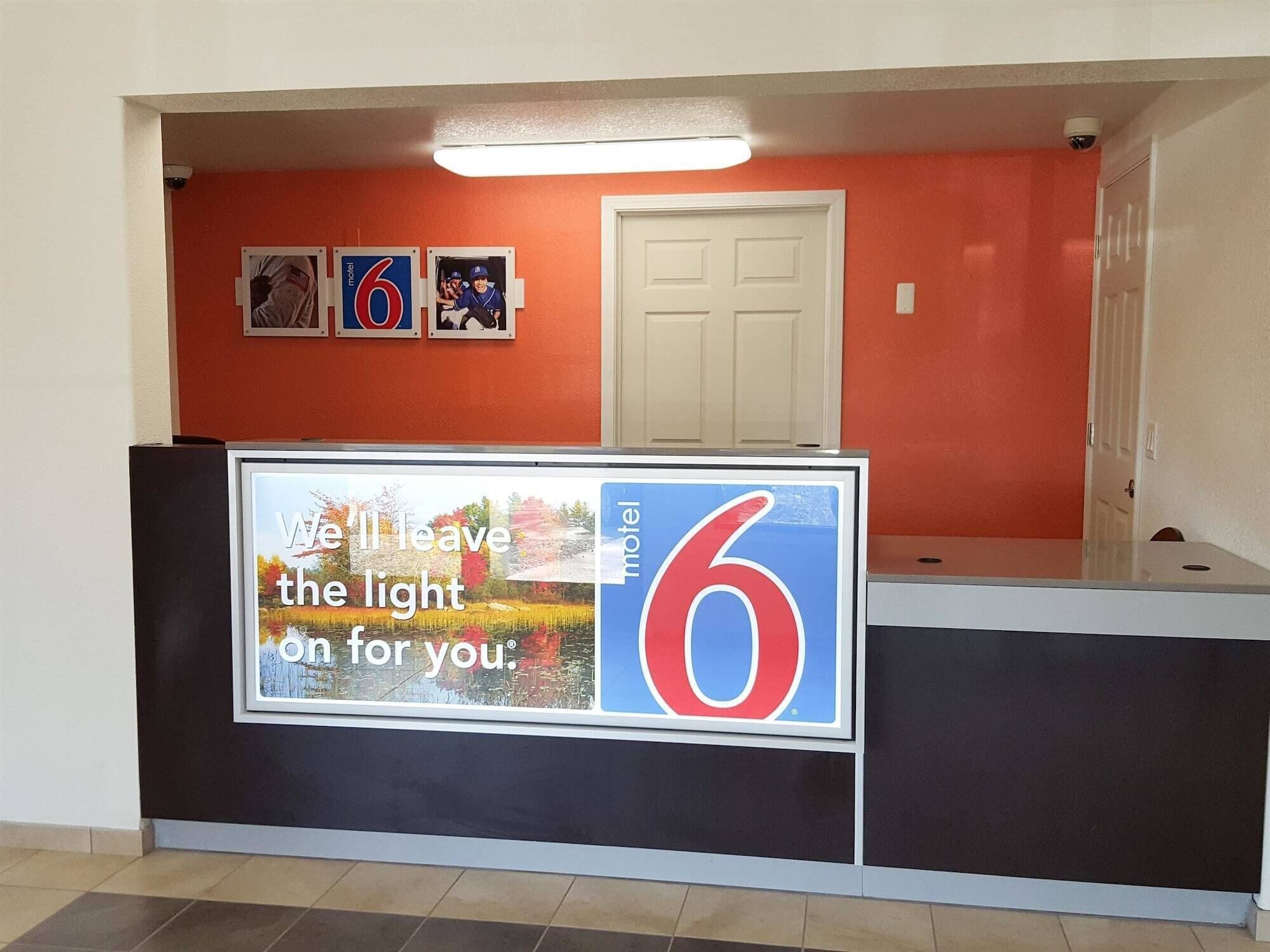 A hotel reception area with a prominent number '6' sign, a white door, and a framed picture of a baseball player.