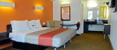 Habitación de hotel con cama, escritorio, silla, mesita, espejo y baño con lavamanos y espejo.