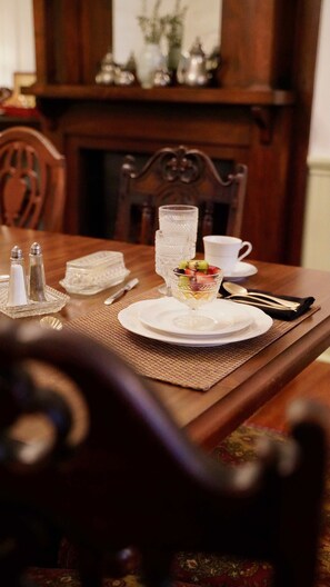 A dining table set with white plates, a glass dessert bowl, salt and pepper shakers, a water glass, and cutlery.