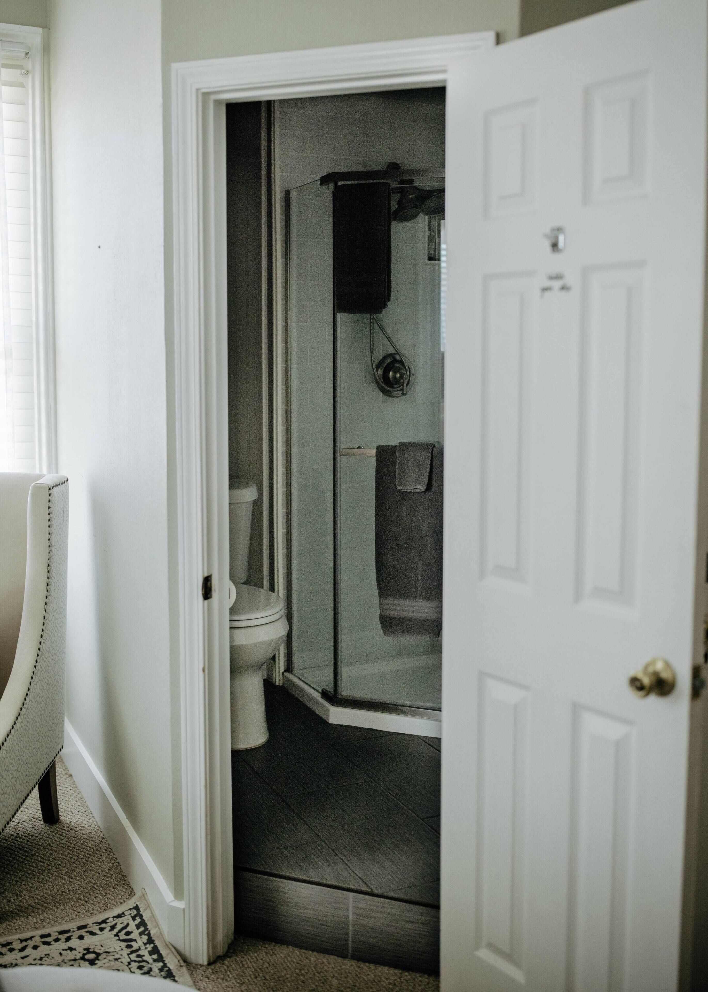 A narrow hallway leading to a bathroom with a toilet, a shower, and a towel rack.