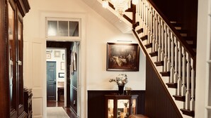 A grand staircase with wooden railings and a chandelier, leading to a room with a fireplace and a framed picture on the wall. - Blue Ridge Inn Bed & Breakfast (Blue Ridge)