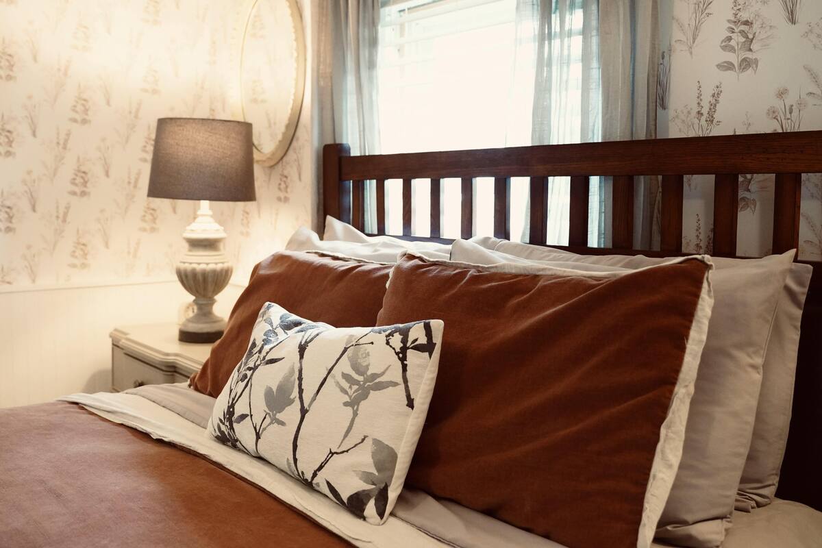 Uma cama bem arrumada com roupa de cama marrom e branca, um travesseiro floral e uma cabeceira de madeira.