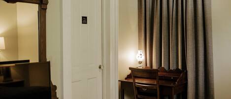 Une chambre d’hôtel avec un lit, un bureau et une chaise, un téléviseur posé sur une commode, une porte avec une pancarte et des rideaux.