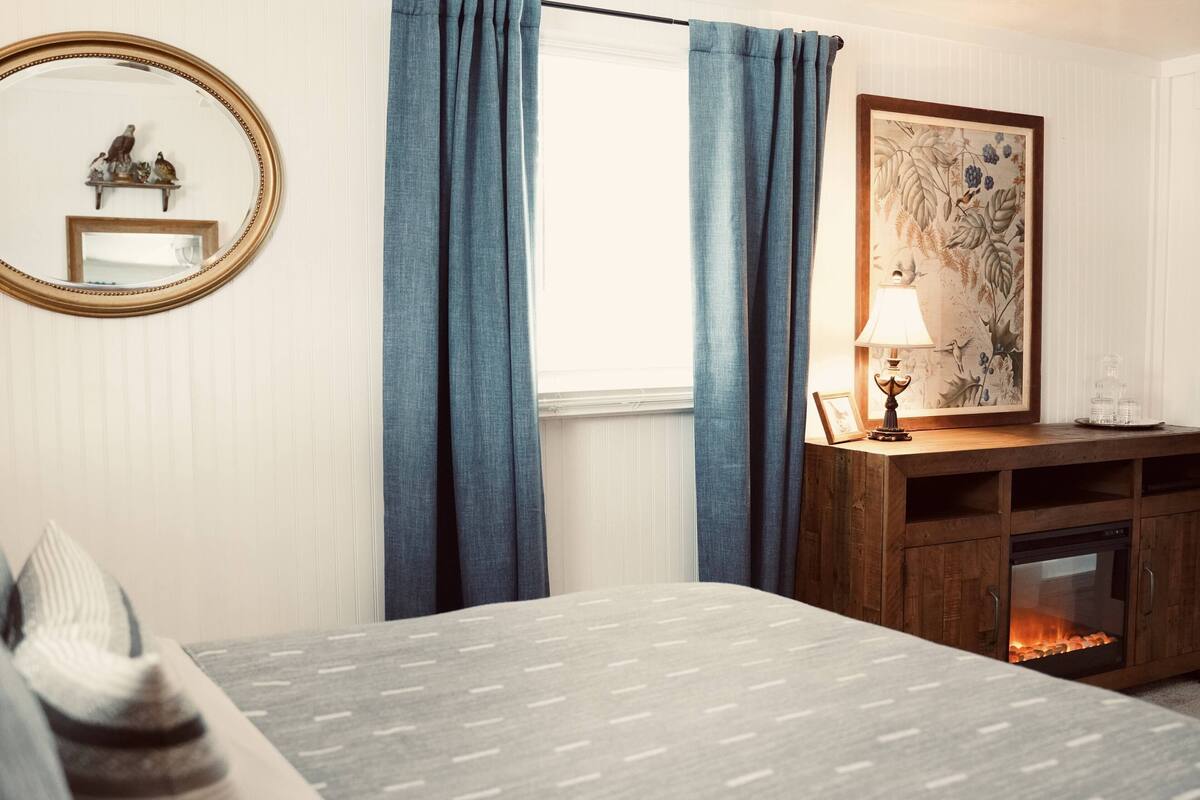 Um quarto com cama, lareira, espelho e um quadro na parede.