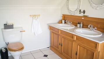 A bathroom with a toilet, two sinks, wooden cabinets, and a mirror.