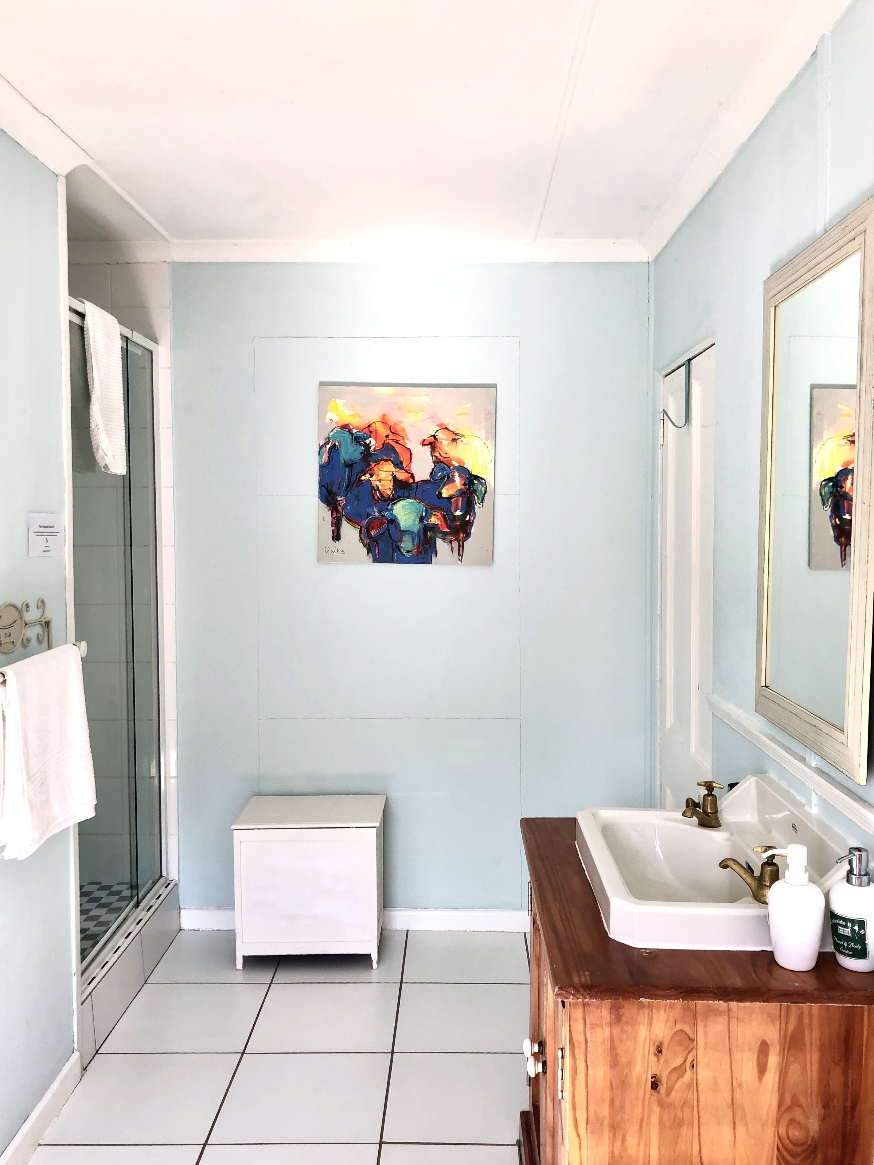 Une salle de bain avec une douche, un lavabo avec un meuble-vasque en bois, un grand miroir et un tableau accroché au mur.