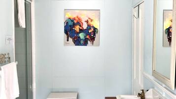 Un baño con ducha, un lavabo con tocador de madera, un espejo grande y un cuadro en la pared.