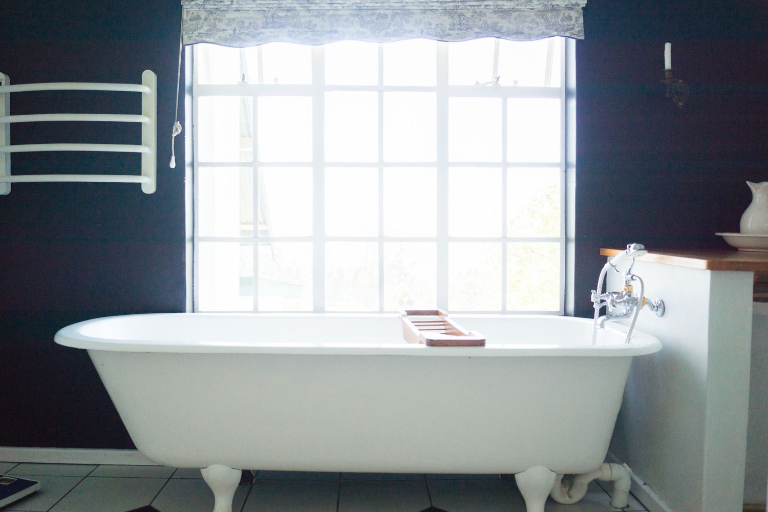 A bathroom with a freestanding bathtub, a window with a lace curtain, and a towel rack on the wall.