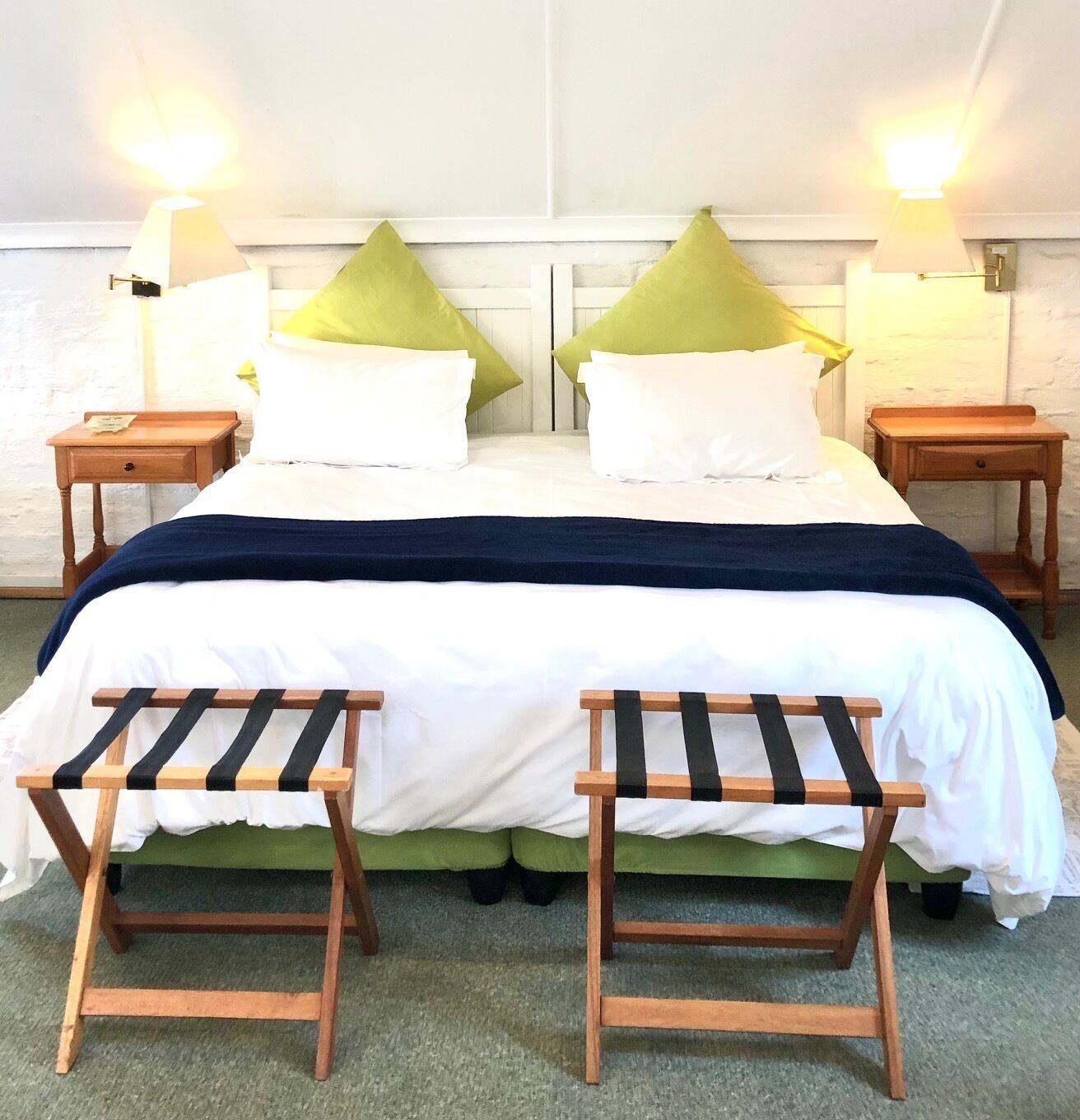 A double bed with a white and navy blue bedspread, two green pillows, and two wooden nightstands with lamps.