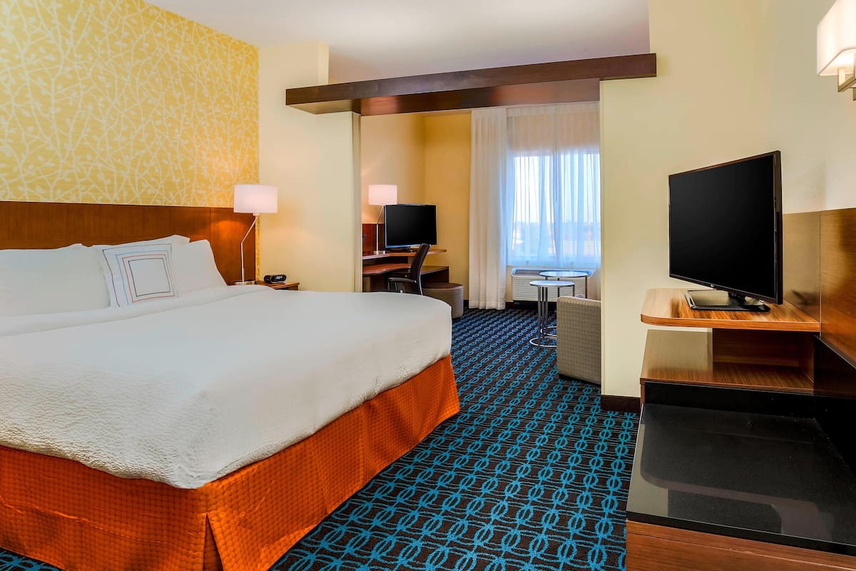 A hotel room with a large bed, a desk with a computer, a television, and a bathroom visible through an open door.