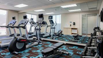Un gimnasio con cintas de correr, elípticas, una banca y máquinas de pesas.