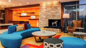 A modern lounge area with a curved blue sofa, a stone fireplace, and a reception desk with 'Connect & Print' signage. - Fairfield Inn & Suites by Marriott Snyder (Snyder)