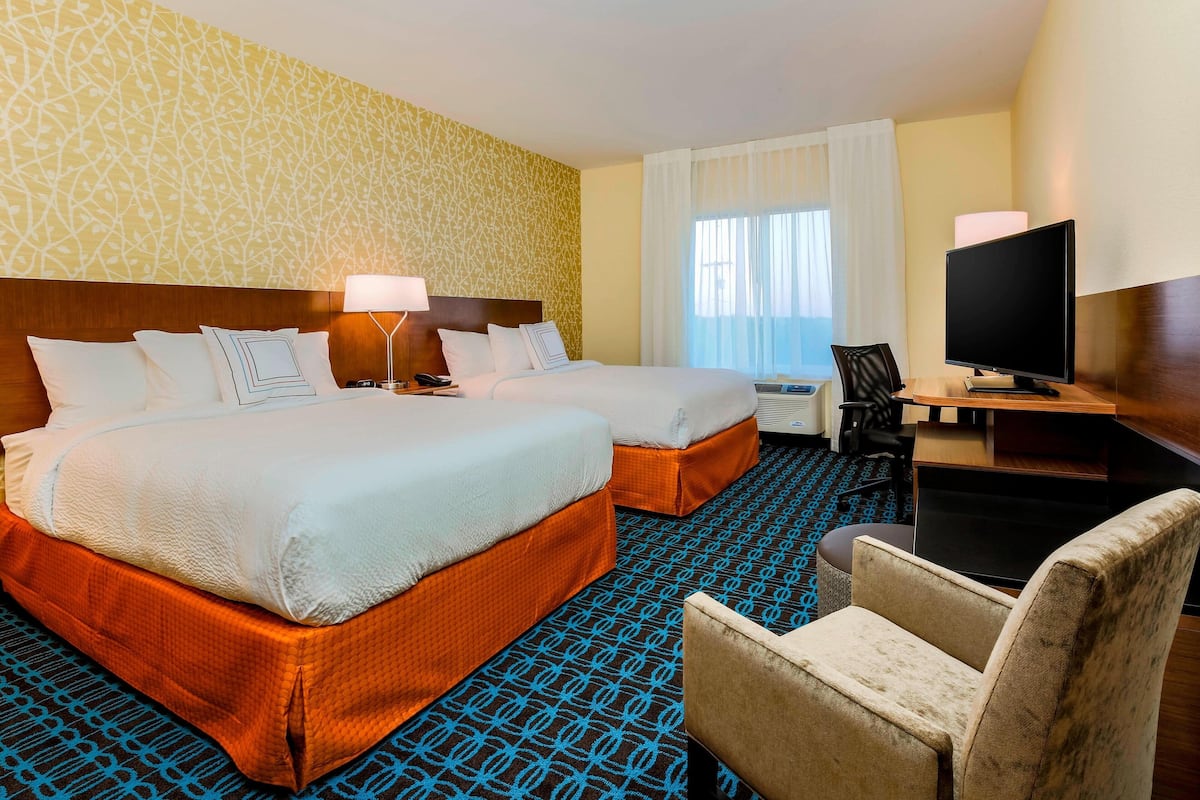 A hotel room with two beds, a desk with a TV, and a chair.