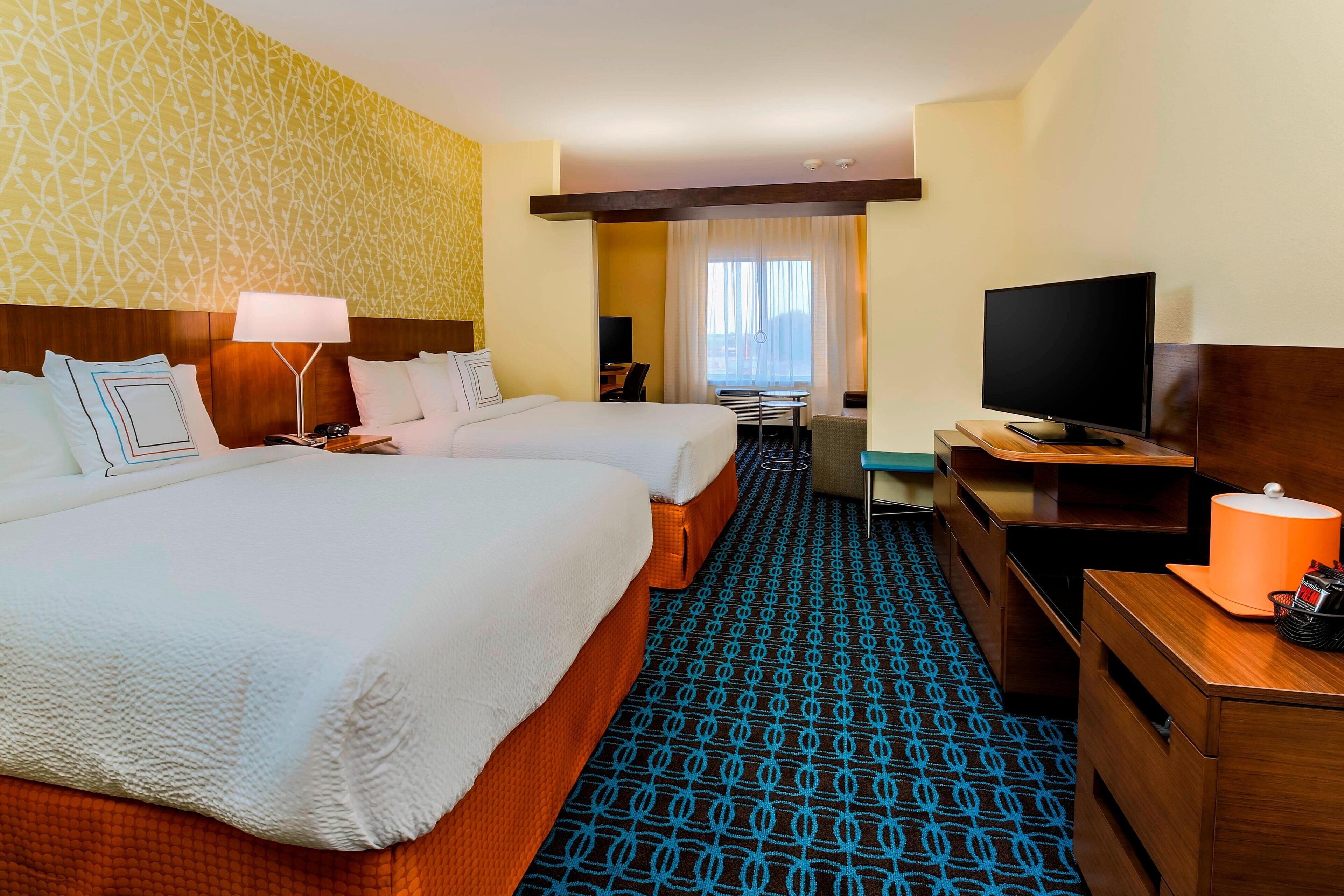 A hotel room with two beds, a desk, a television, and a window with curtains.