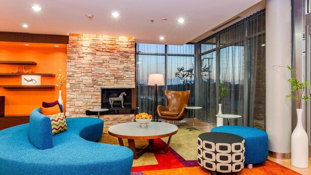 A modern living room with a stone wall, blue seating, a round coffee table, and a fireplace. - Fairfield Inn & Suites by Marriott Snyder (Snyder)